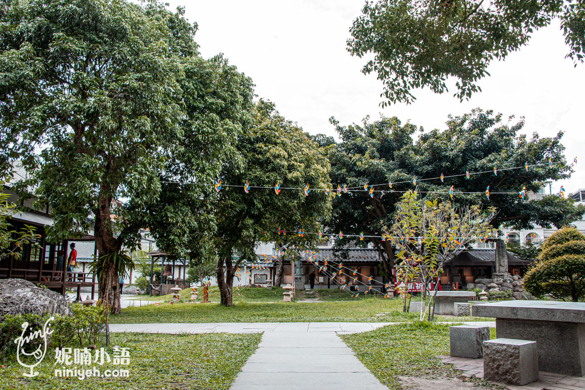 吉安慶修院綠意盎然的日式庭園全景，中央設有石板步道與石桌椅，樹木之間拉起裝飾用的彩色小風箏線
