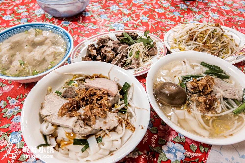 賴新魁麵館的招牌美食：湯粄條加肉片、滷蛋與蔥油搭配，再加上小菜如大骨肉、燙青菜及餛飩湯，豐富的傳統客家美食擺放在紅色花紋桌布上。