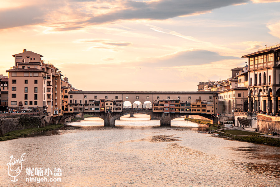 佛羅倫斯老橋（Ponte Vecchio）在黃昏時分的美麗景色，橘紅色的晚霞映照在阿諾河水面上，橋上的古老建築與珠寶店展現出佛羅倫斯獨特的歷史風情，完美捕捉文藝復興時期的浪漫氛圍，是佛羅倫斯經典地標之一