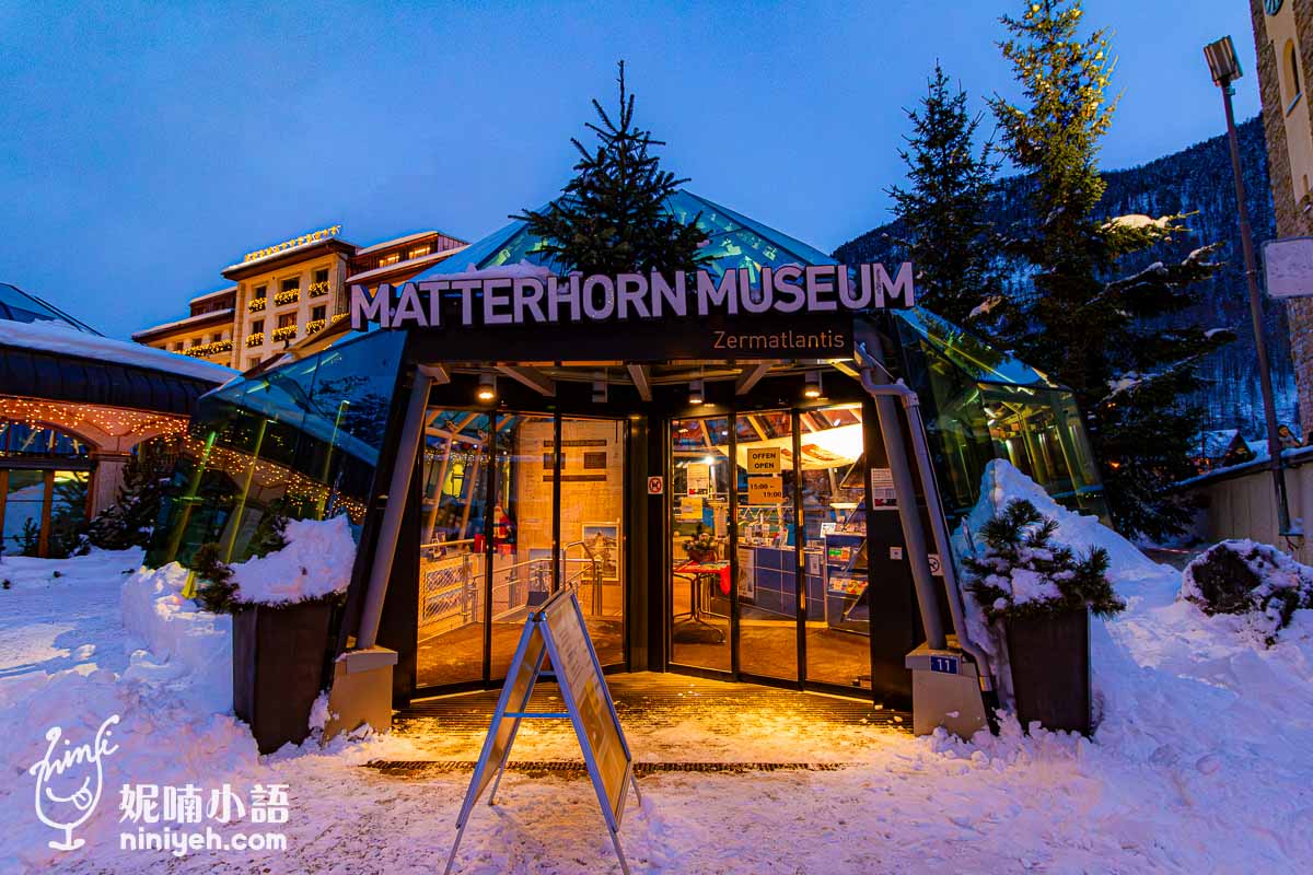 這張圖片展示了馬特洪峰博物館的入口，位於策馬特，是該地區的著名景點。博物館在黃昏時分燈光亮起，吸引了遊客參觀馬特洪峰的歷史與文化背景。