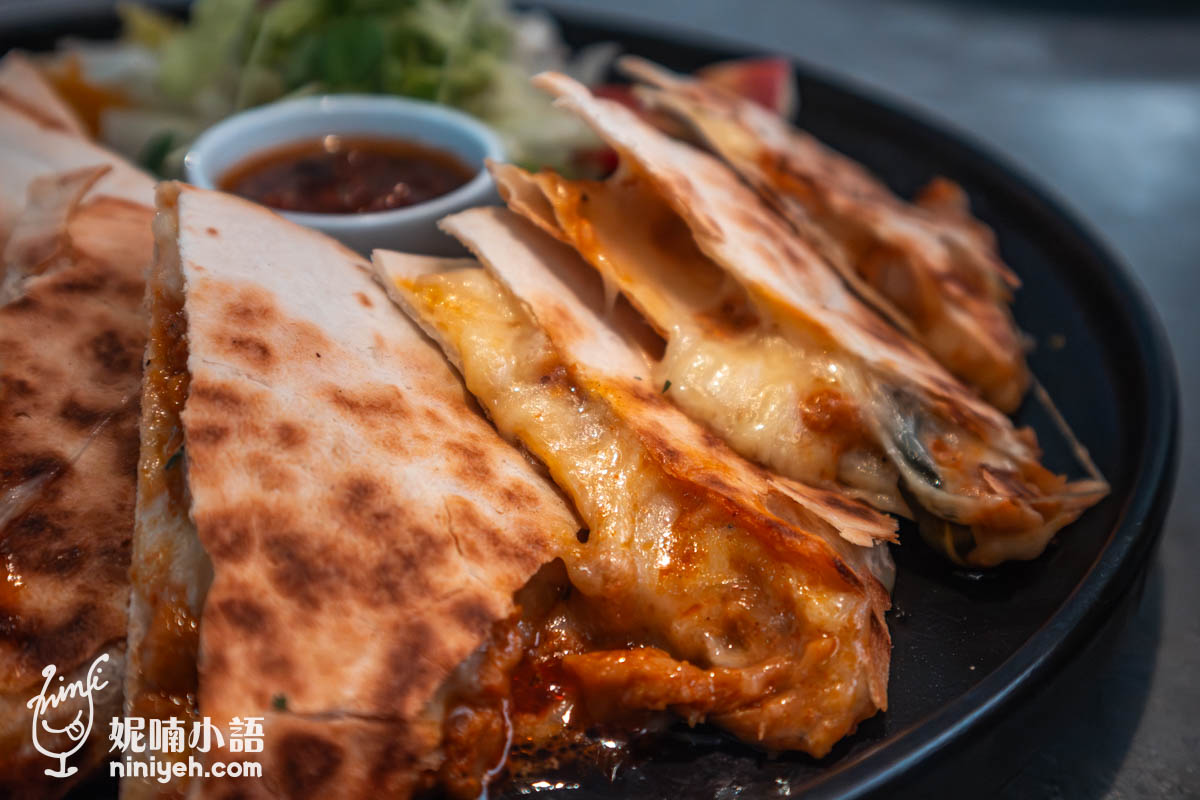 特寫拍攝墨西哥薄餅,餅皮金黃酥脆、起司融化溢出,內餡夾有肉醬與蔬菜,背景可見沾醬與生菜沙拉,呈現誘人的拉絲口感。