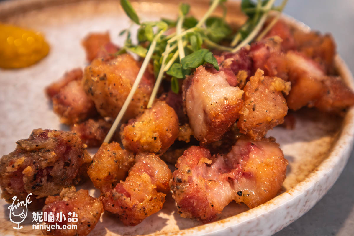 特寫酥炸德國豬腳,外皮金黃酥脆、內層肉質鮮嫩多汁,搭配綠色芽菜點綴,旁邊有一小團黃芥末醬作為佐料。