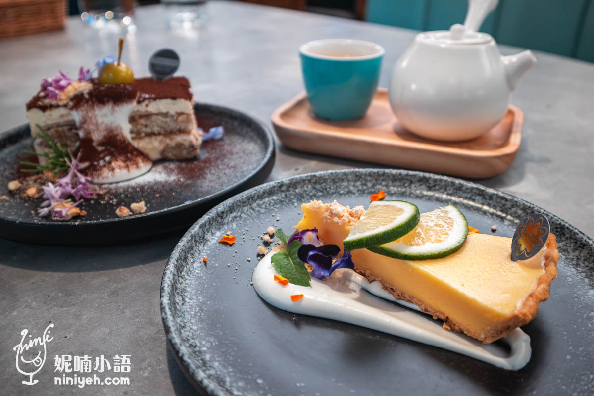 餐桌上的甜點與茶飲,前景為檸檬派搭配鮮奶油與花瓣點綴,後方為提拉米蘇蛋糕,旁邊放有茶壺與茶杯,擺盤精緻。