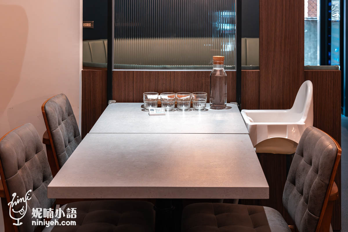 禾多餐酒館室內雙人座位,灰色軟墊椅搭配兩張相連的長方形桌,桌上擺有玻璃水壺與杯子,旁邊設有白色兒童座椅,環境溫馨且親子友善。