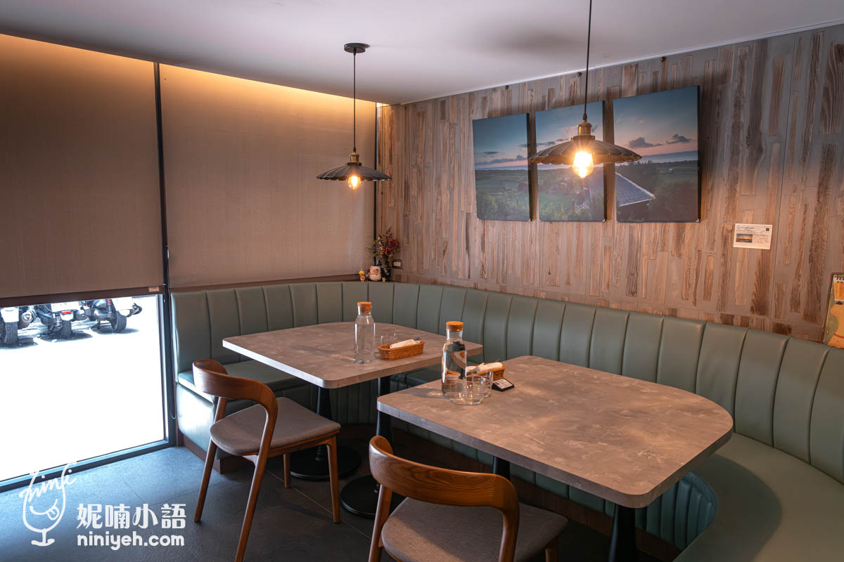 禾多餐酒館室內座位區,綠色弧形沙發搭配兩張長方形木質桌,牆面裝飾著三幅風景照片,吊燈散發暖色光線,氛圍溫馨舒適。