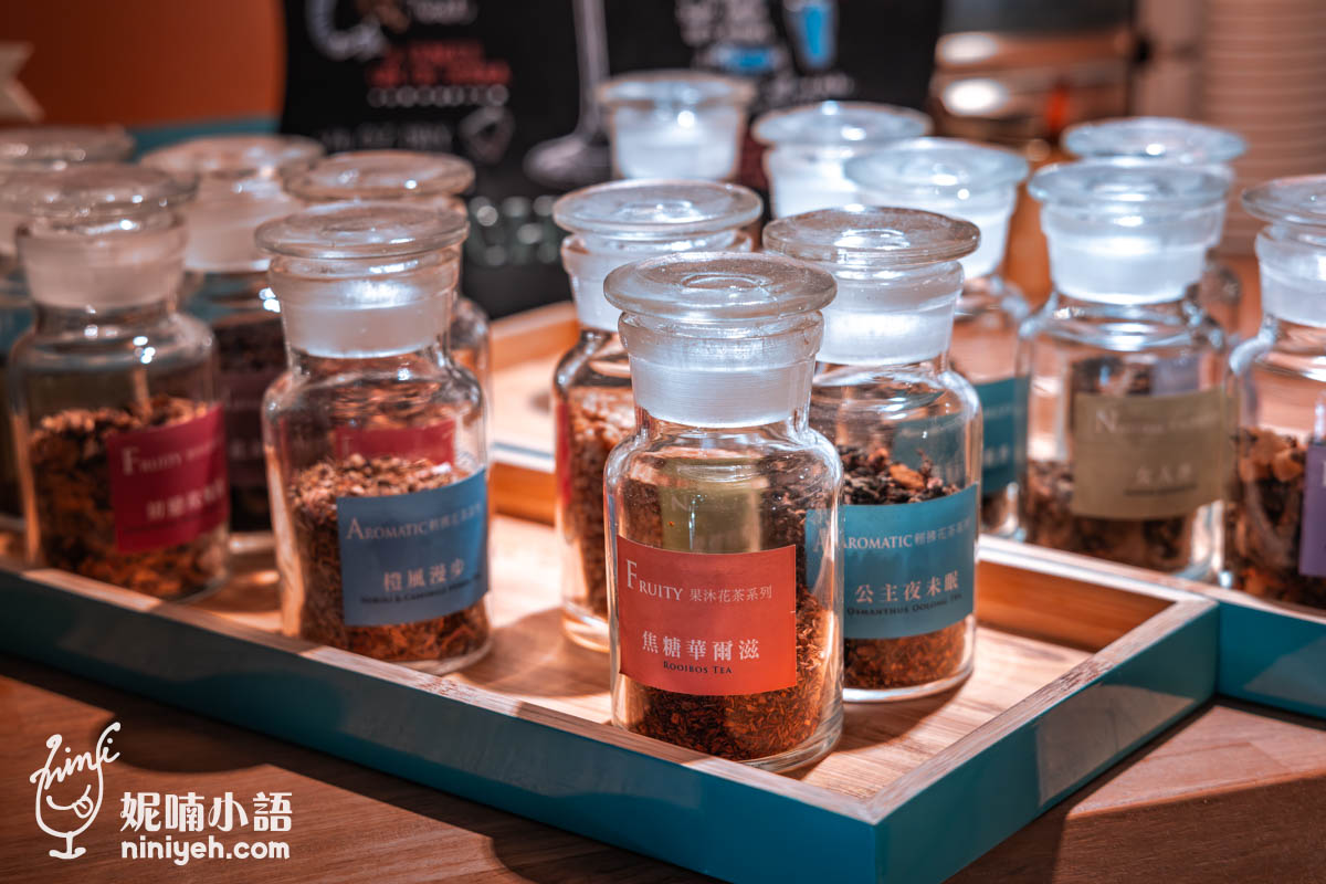 禾多餐酒館自家品牌花草茶展示，數個透明玻璃瓶中裝有不同種類的茶葉，瓶身貼有標籤如焦糖蜂醋漿與公主夜未眠，整齊擺放在木盤上供顧客聞香挑選。