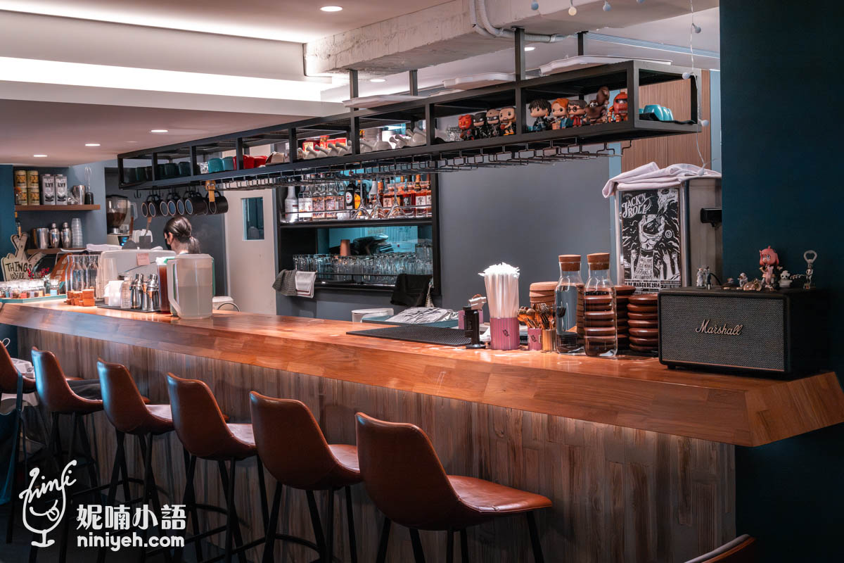 禾多餐酒館(小巨蛋店)室內吧台區,木質長桌搭配多張高腳椅,吧台上擺放飲品器具與Marshall音響,背景架上擺滿公仔與酒瓶,環境溫馨且具設計感。