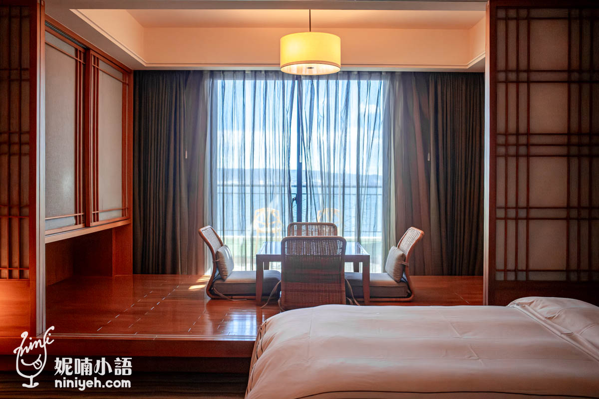 這張圖片展現了一個融合傳統日式美學與現代舒適感的室內空間，其核心在於營造一種寧靜且平衡的居住氛圍。畫面中以溫潤的木質色調為主軸，透過精緻的和室榻榻米區域與矮桌座椅，將視覺焦點引導至遠方遼闊的湖光山色。整體設計運用了光影與材質的交織，利用半透明的紗簾過濾自然光，使室內充滿柔和的暖意，展現出一種優雅的禪意生活哲學。這個空間的配置不僅是為了休憩，更是為了讓居住者能在這純粹的環境中，達到身心靈的放鬆與沉澱。