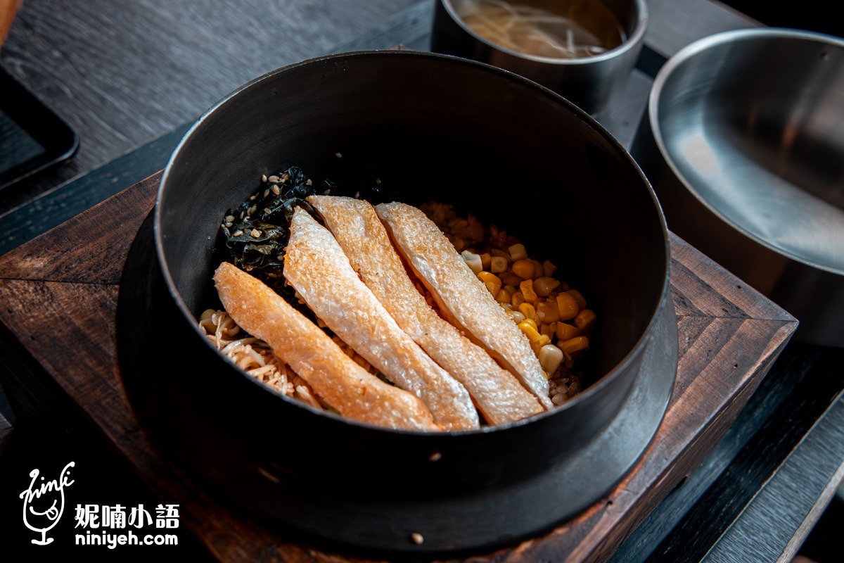「金美麗人 韓國直火釜飯專賣店」每日限量供應的海鹽烤鮭魚肚釜飯特寫,鐵鍋內鋪滿經炙烤後呈現迷人焦糖色澤、油脂豐美的鮭魚肚肉片。