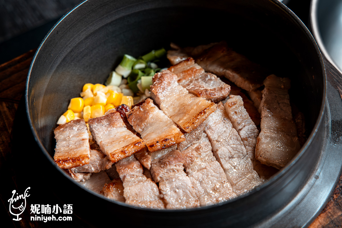 「金美麗人」現點現煮的韓式五花肉釜飯側面特寫,烤至微焦、油脂豐厚的海鹽豬五花肉片整齊排列在直火炊煮的暖黃色米飯上,視覺效果飽滿澎派。