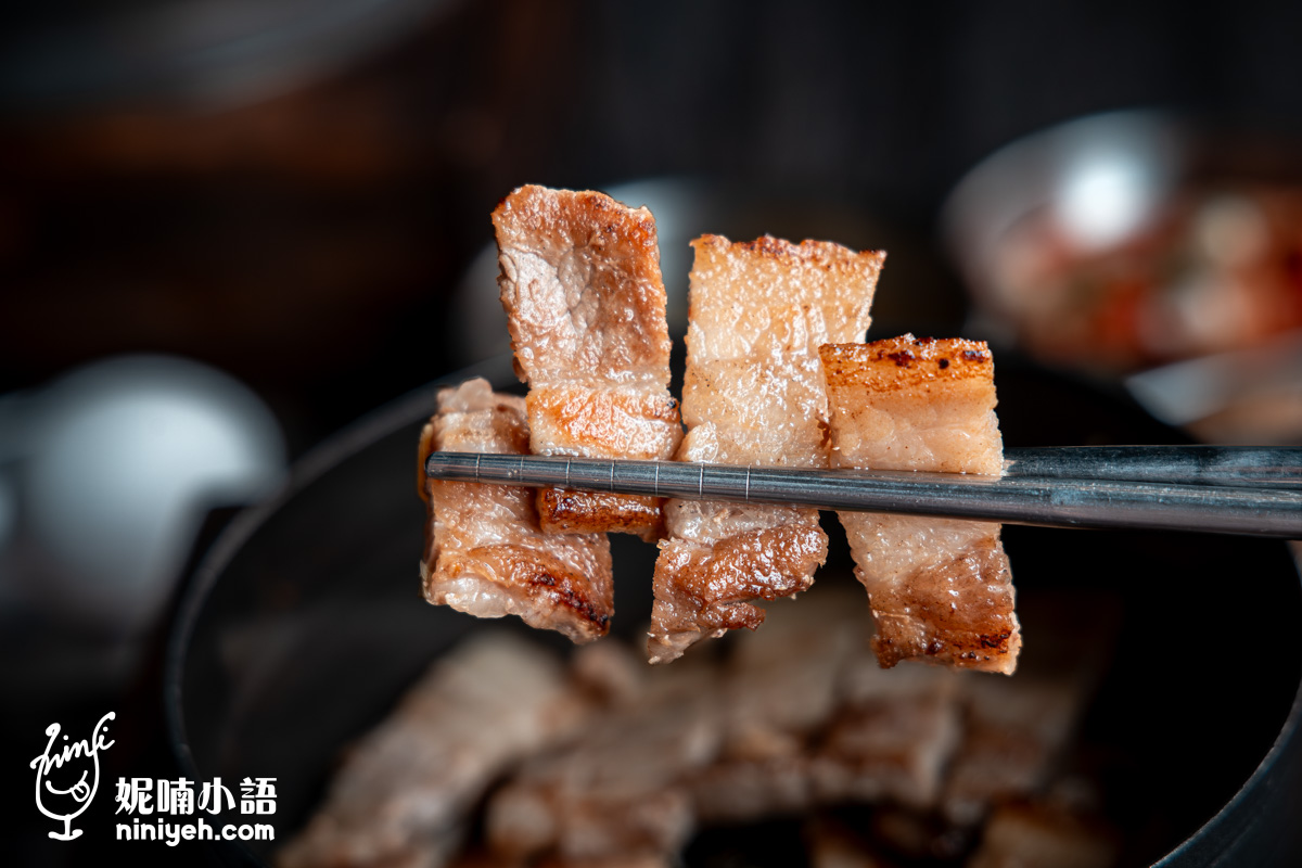 使用筷子夾起台北士林「金美麗人」海鹽烤豬五花釜飯中的厚實五花肉片,金黃焦香的外皮與多汁肉質,展現現烤的美味誘惑。