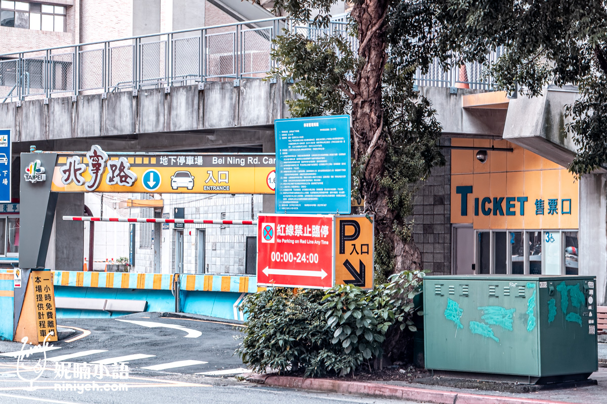 台北松山區北寧路地下停車場入口實景。畫面中可以看到黃色牌樓上的中文「北寧路地下停車場入口」與英文「Bei Ning Rd. Car Park Entrance」字樣，旁邊是「Ticket 售票口」指示牌和一個綠色變電箱