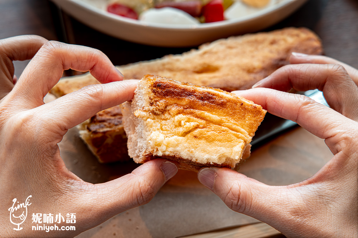 雙手撕開香蒜奶酥麵包的特寫鏡頭。手指抓著剛撕下的一小塊麵包,清晰展現出內部蓬鬆細緻的白色麵包組織,以及表層厚實、濕潤融化的香蒜奶酥內餡,背景為砧板上剩餘的麵包與沙拉。