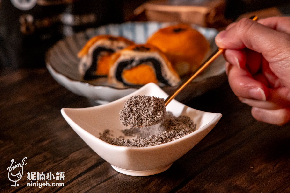 手持金湯匙舀起芝初8倍細高鈣黑芝麻粉特寫,展現如雪花般細緻的粉末質地,背景搭配切開的芝麻蛋黃酥