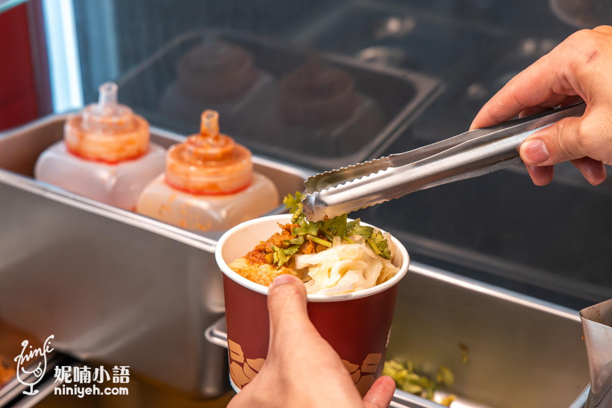 老闆用夾子在裝有臭豆腐的紙碗中放入香菜等配菜