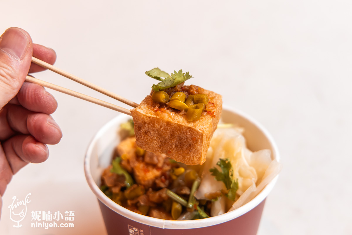 竹籤夾起一塊頂端堆疊酸豇豆與香菜的薄片臭豆腐