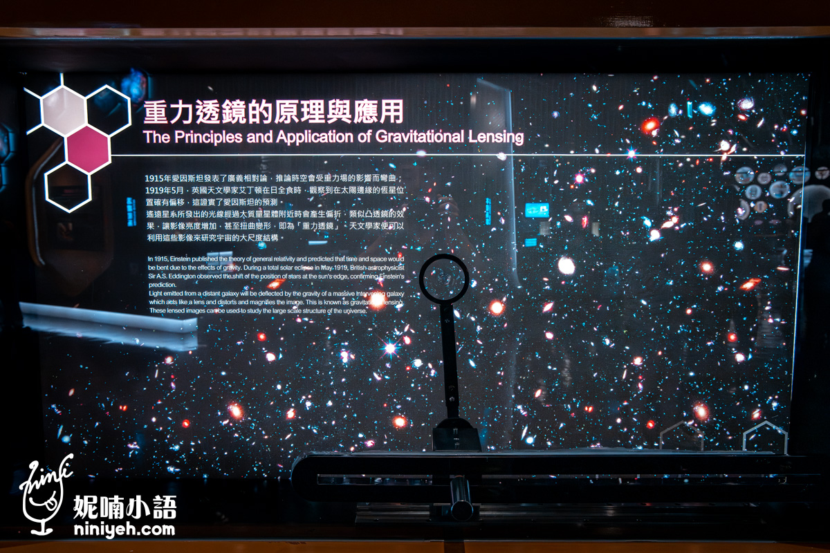 重力透鏡的原理與應用」展板，前方放置了真實的放大透鏡，後方背景展示了因重力扭曲的星系影像，非常有視覺張力